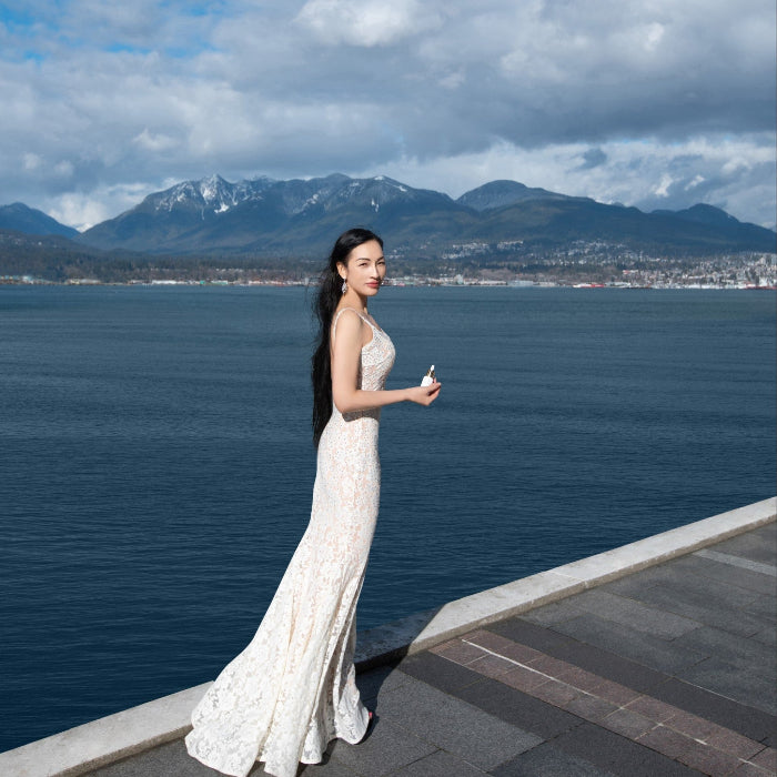 Xiaura FOUNDER MICHELLE in a white dress standing by a waterfront with mountains in the background.