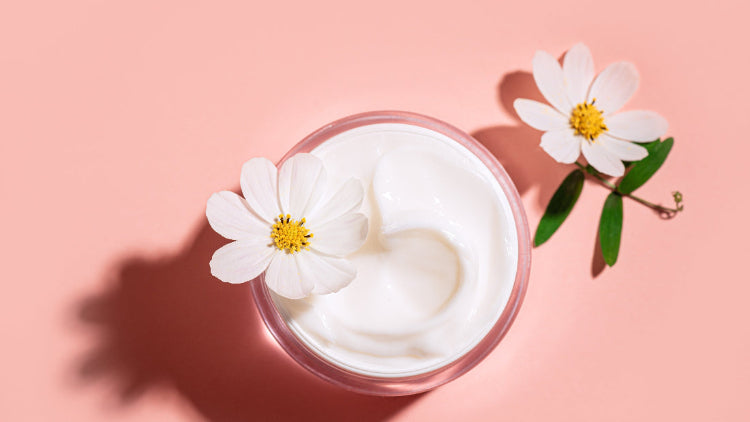 Jar of white cream with a white flower on a pink background