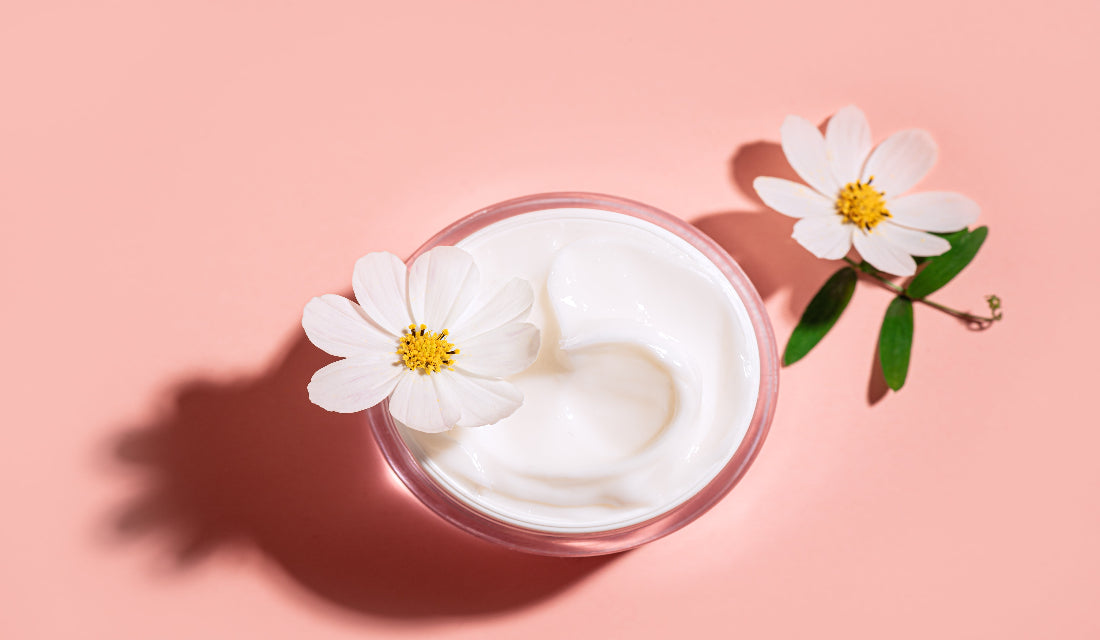 Jar of white cream with a white flower on a pink background