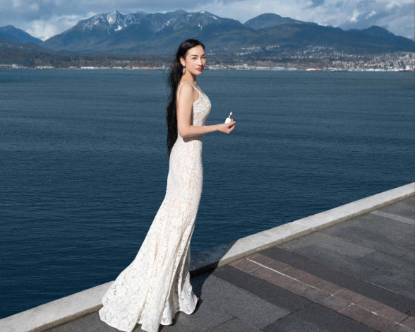 Woman in a white dress standing by a waterfront with mountains in the background